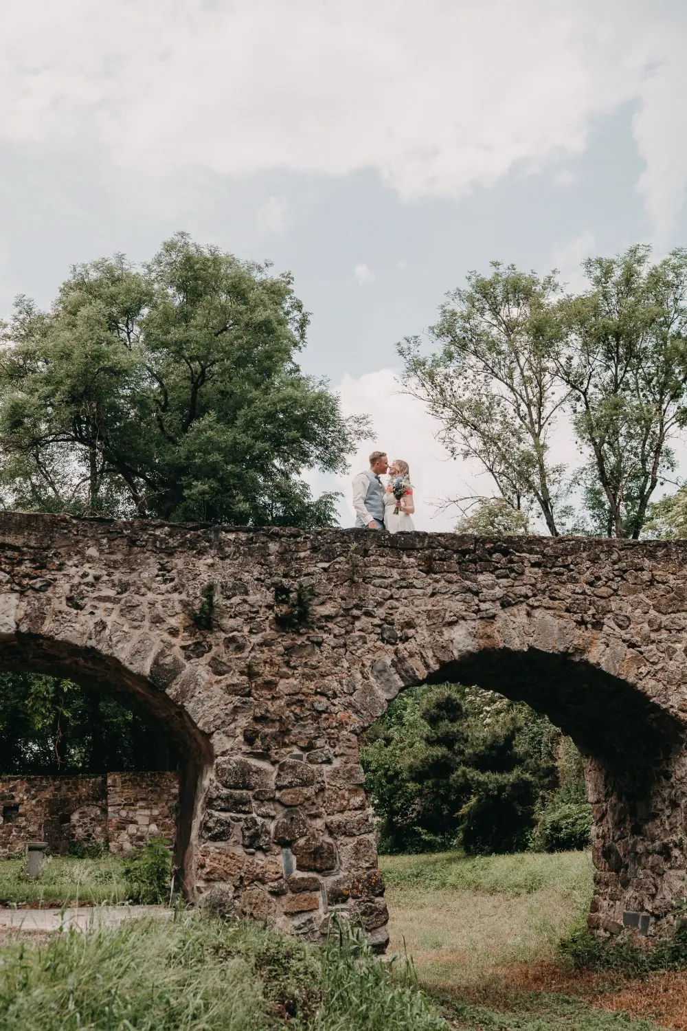 Brautpaar auf einer alten Steinbrücke im Grünen