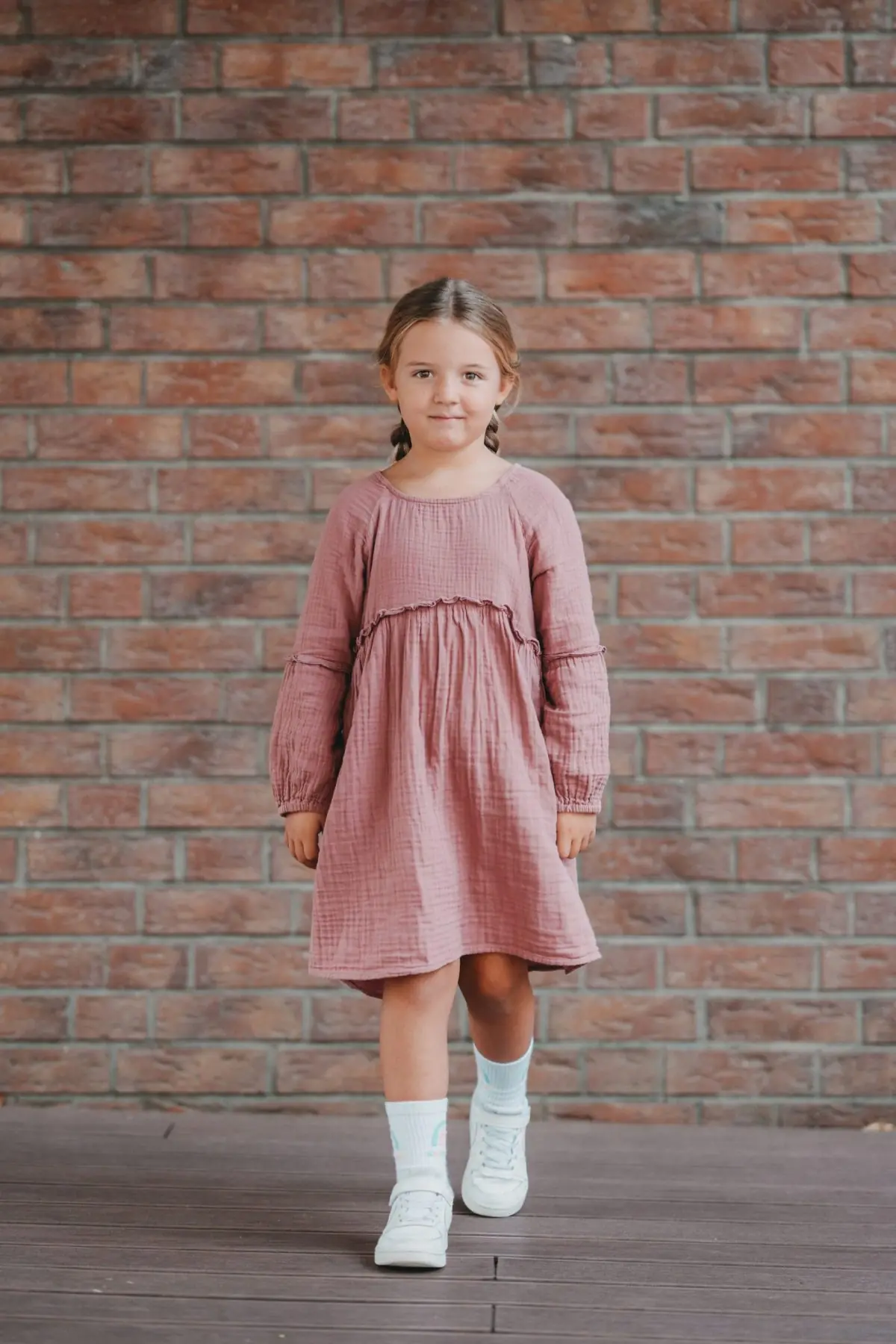 Mädchen im rosa Kleid vor einer Ziegelwand