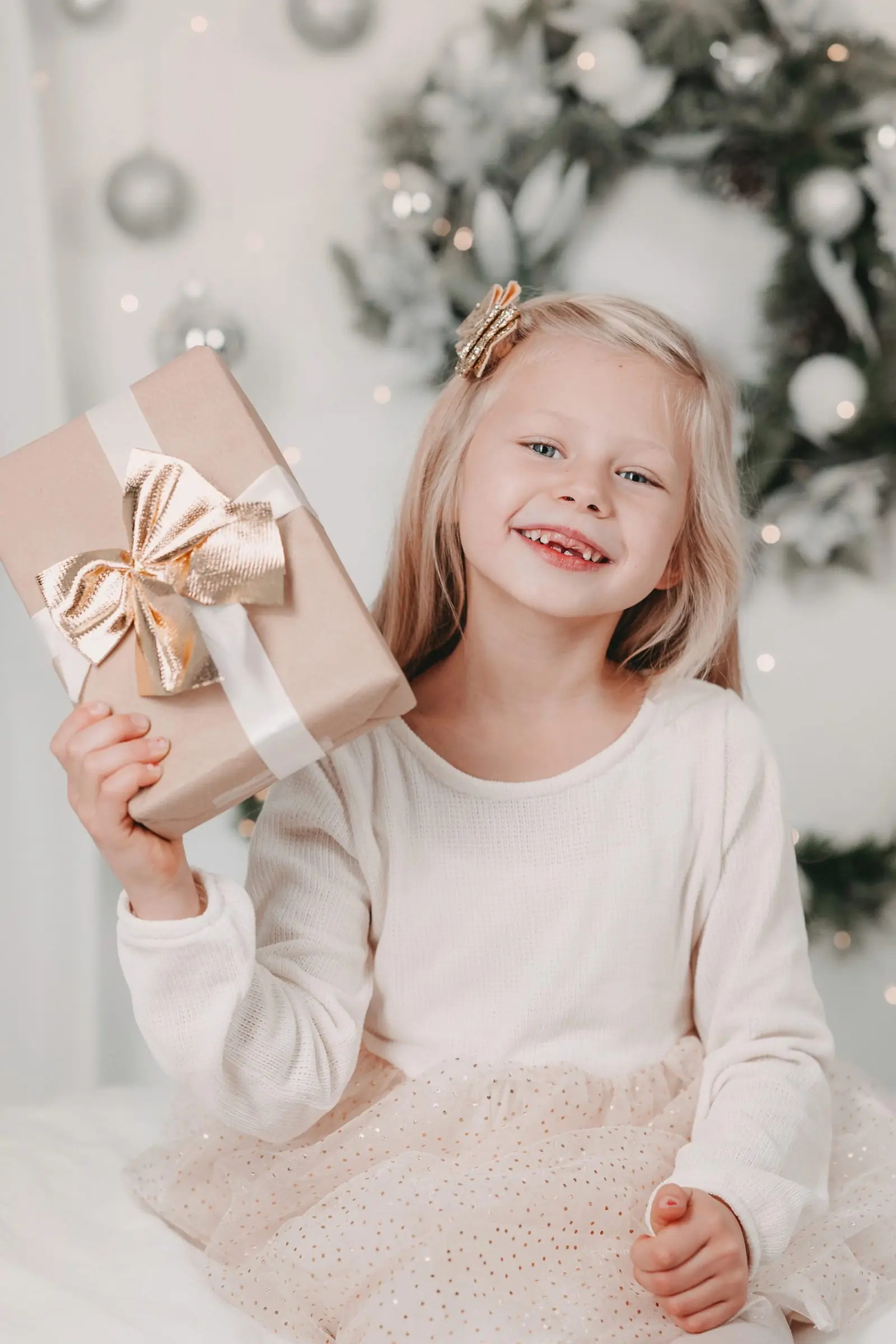 Mädchen hält lachend ein Geschenk vor einem Weihnachtskranz