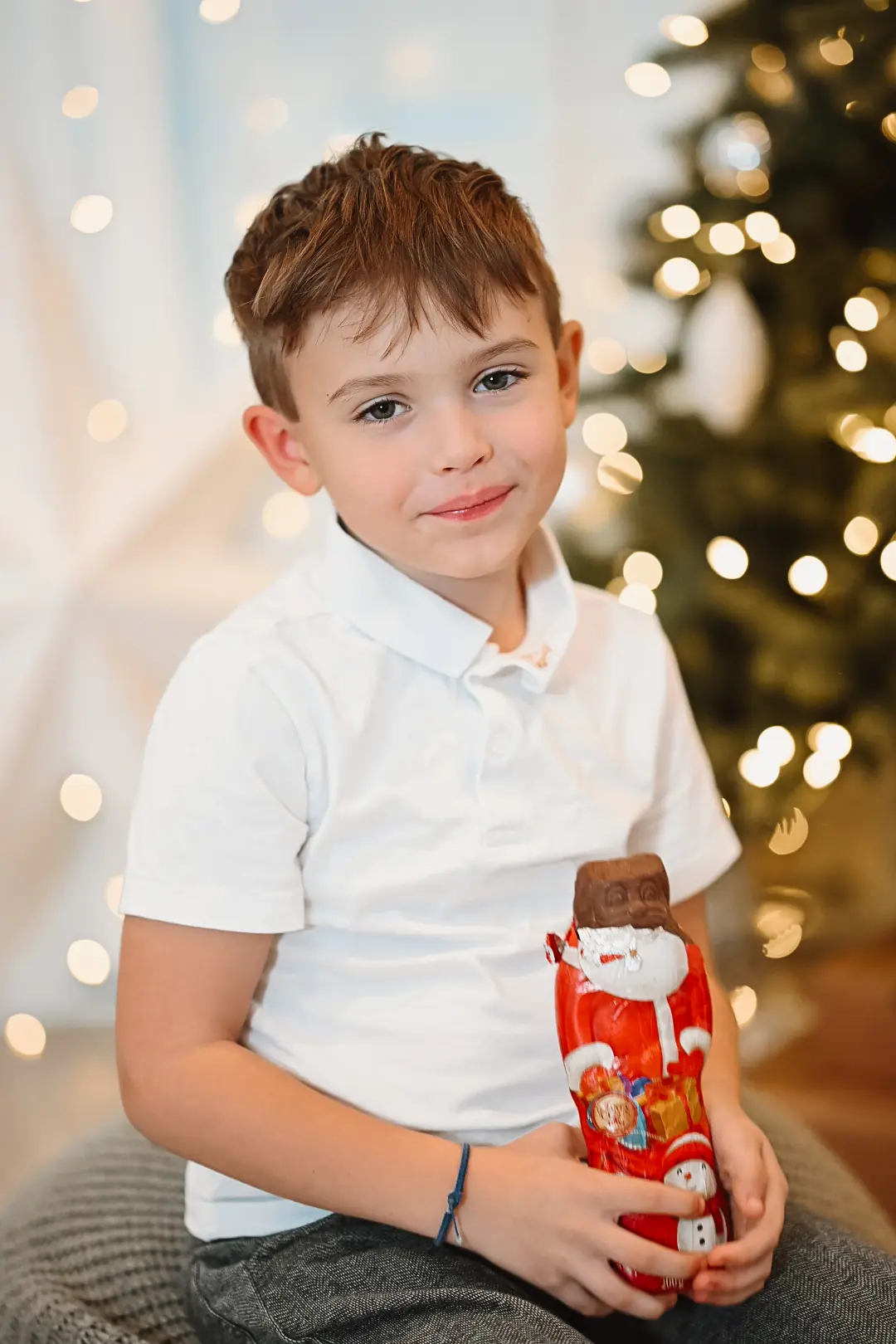 Junge mit Schoko-Weihnachtsmann vor dem Tannenbaum
