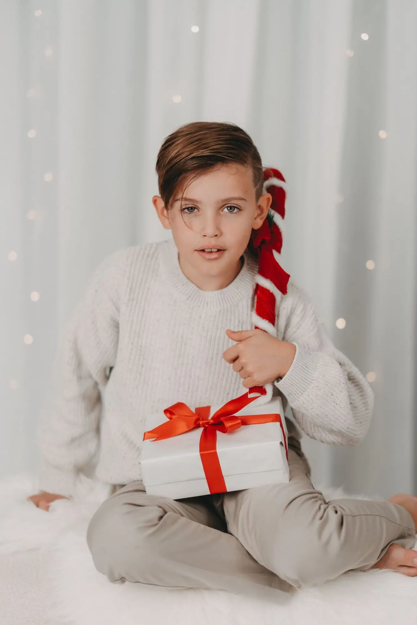 Junge mit Geschenk und Zuckerstange vor Lichtervorhang