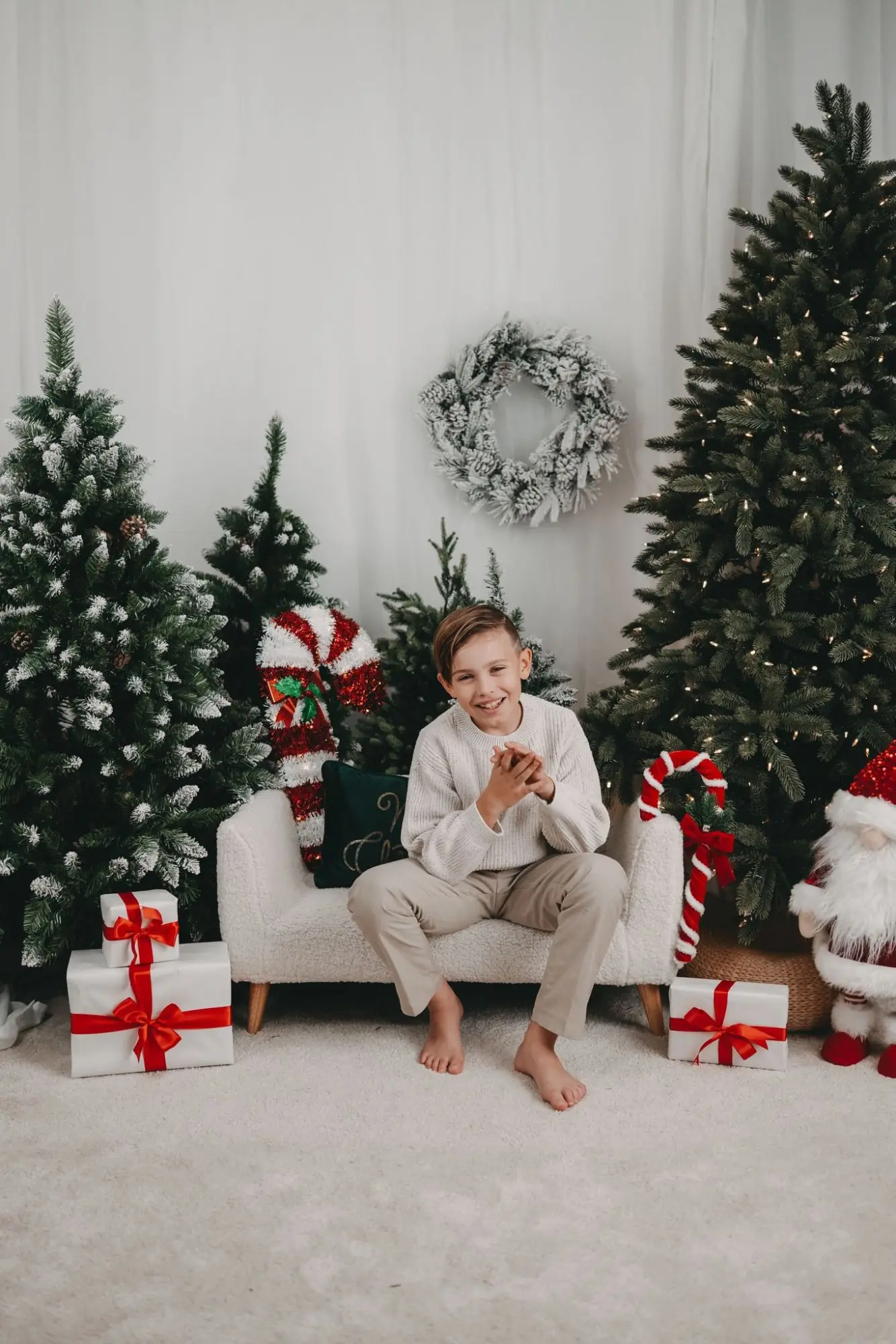 Junge sitzt lachend auf dem Sofa zwischen Tannen, Zuckerstangen und Geschenken