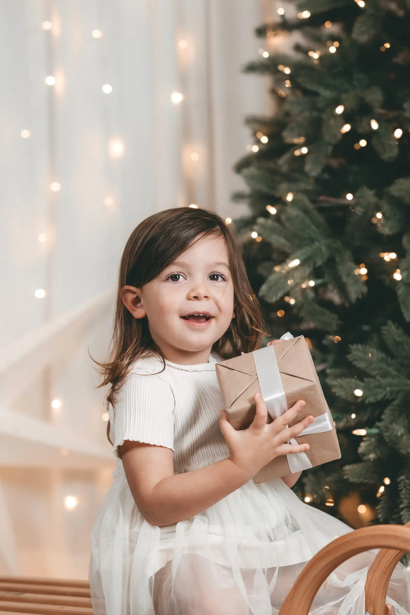 Kleines Mädchen mit Geschenk vor dem Weihnachtsbaum